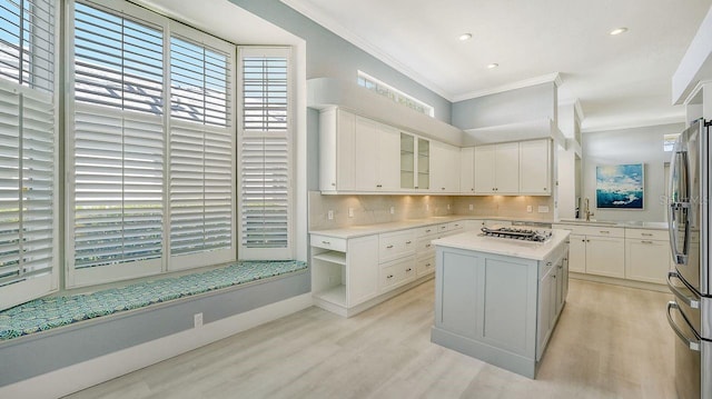 kitchen featuring white cabinetry, stainless steel appliances, tasteful backsplash, ornamental molding, and a kitchen island