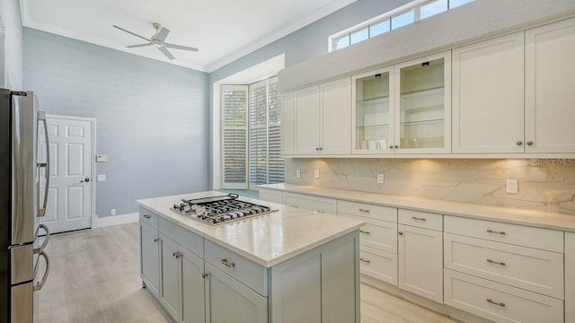 kitchen with crown molding, a center island, appliances with stainless steel finishes, ceiling fan, and backsplash