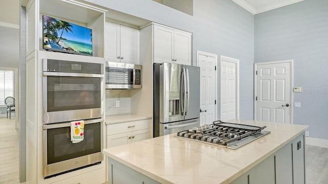 kitchen with light stone counters, crown molding, a center island, appliances with stainless steel finishes, and white cabinets