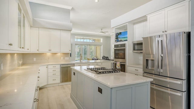 kitchen with light stone counters, stainless steel appliances, a kitchen island, and white cabinets