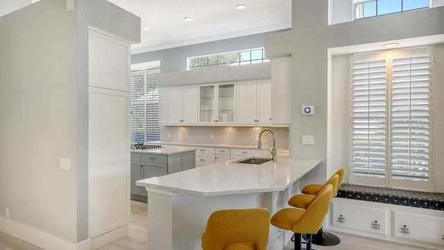 kitchen with a kitchen bar, sink, tasteful backsplash, kitchen peninsula, and white cabinets