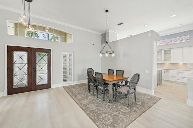 dining space featuring an inviting chandelier, crown molding, french doors, and light wood-type flooring