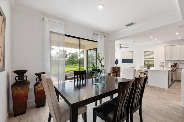 dining space featuring light wood-type flooring, ornamental molding, sink, and ceiling fan