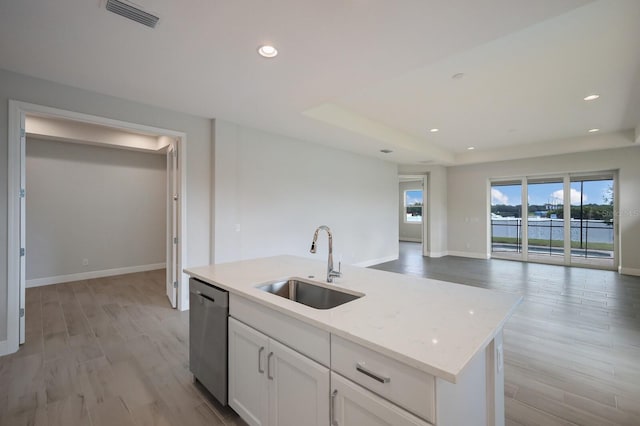 kitchen with white cabinetry, sink, a kitchen island with sink, stainless steel dishwasher, and light stone countertops