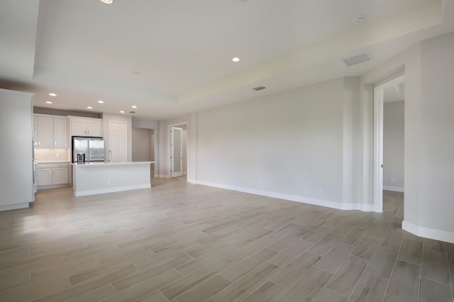 unfurnished living room with sink, light hardwood / wood-style floors, and a tray ceiling