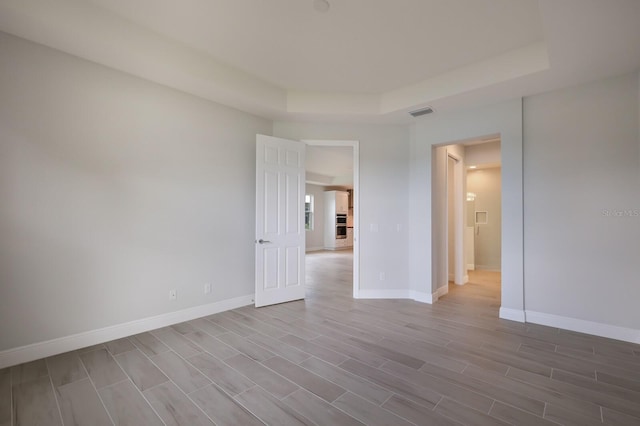 empty room featuring a tray ceiling and light hardwood / wood-style flooring