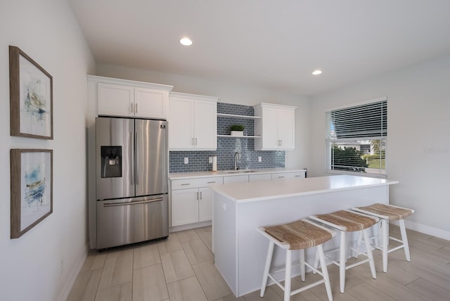 kitchen with stainless steel refrigerator with ice dispenser, sink, a kitchen island, decorative backsplash, and white cabinets