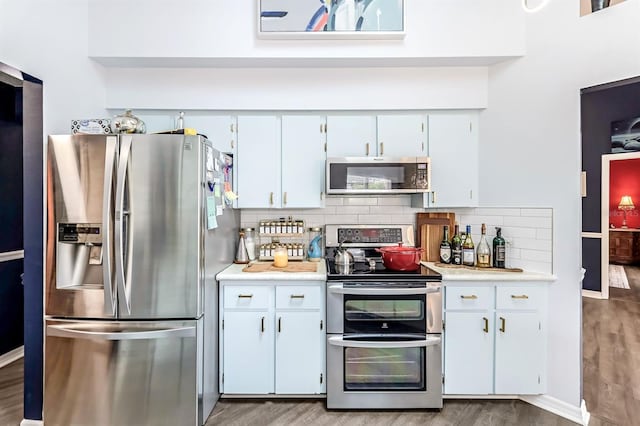 kitchen with appliances with stainless steel finishes, hardwood / wood-style flooring, backsplash, and white cabinets