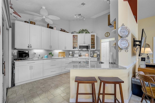 kitchen featuring white cabinetry, backsplash, track lighting, ceiling fan, and sink