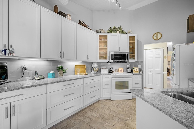 kitchen with white appliances, light tile patterned flooring, light stone countertops, white cabinets, and decorative backsplash