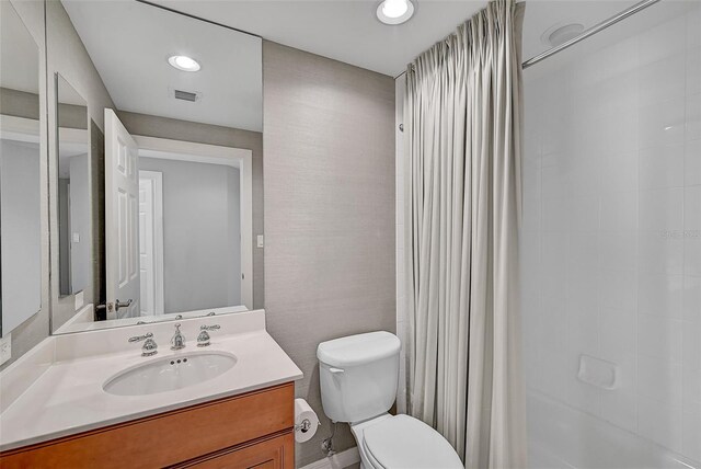 bathroom with tiled shower, vanity, and toilet