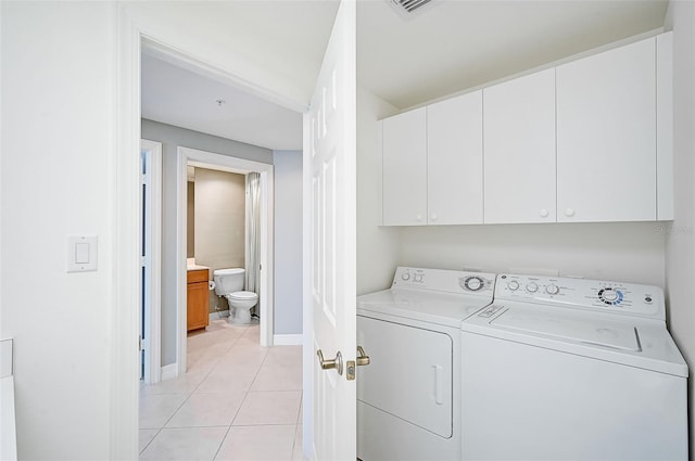 clothes washing area featuring light tile patterned flooring, cabinets, and washing machine and dryer