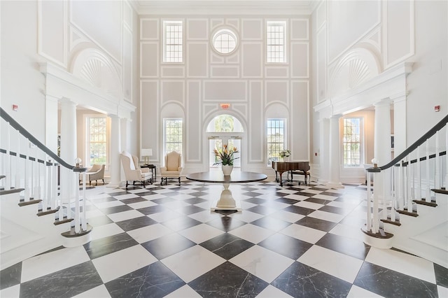 foyer entrance featuring a towering ceiling, a wealth of natural light, and ornate columns