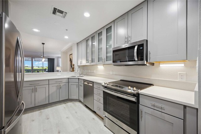 kitchen with stainless steel appliances, hanging light fixtures, gray cabinets, sink, and light hardwood / wood-style floors