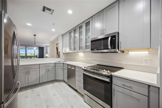 kitchen with appliances with stainless steel finishes, sink, light wood-type flooring, decorative light fixtures, and gray cabinets