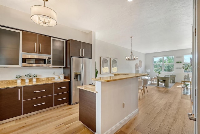 kitchen featuring light hardwood / wood-style flooring, stainless steel appliances, dark brown cabinetry, light stone counters, and decorative light fixtures