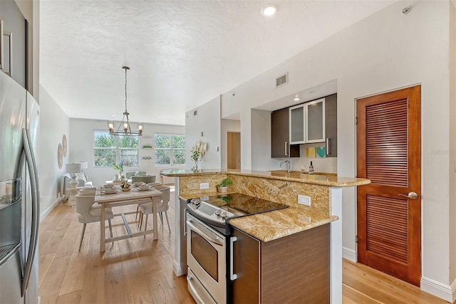 kitchen with light stone counters, appliances with stainless steel finishes, hanging light fixtures, and light wood-type flooring