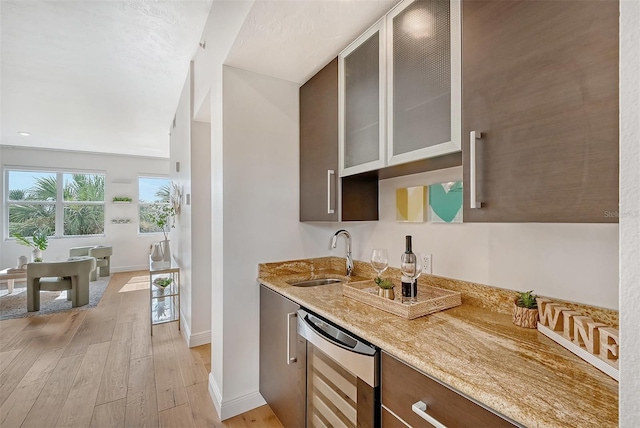 bar featuring sink, dishwasher, light stone counters, wine cooler, and light wood-type flooring