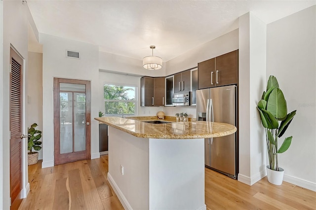 kitchen with a center island, dark brown cabinets, appliances with stainless steel finishes, pendant lighting, and light stone countertops