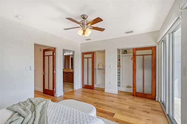 bedroom featuring connected bathroom, ceiling fan, light hardwood / wood-style flooring, and multiple closets