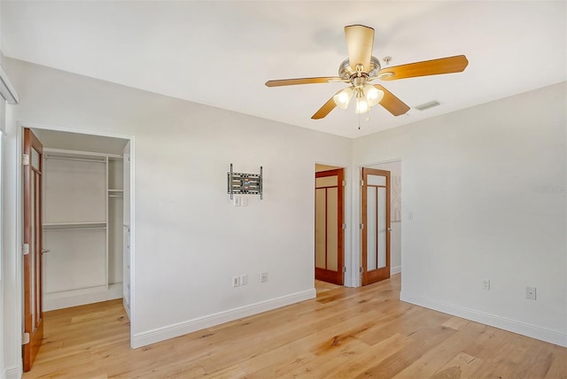 unfurnished bedroom with ceiling fan, a closet, a spacious closet, and light hardwood / wood-style flooring