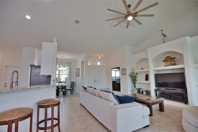 tiled living room with sink, built in features, ceiling fan with notable chandelier, and vaulted ceiling