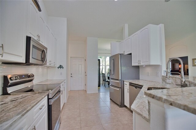 kitchen with appliances with stainless steel finishes, light stone counters, white cabinets, and tasteful backsplash