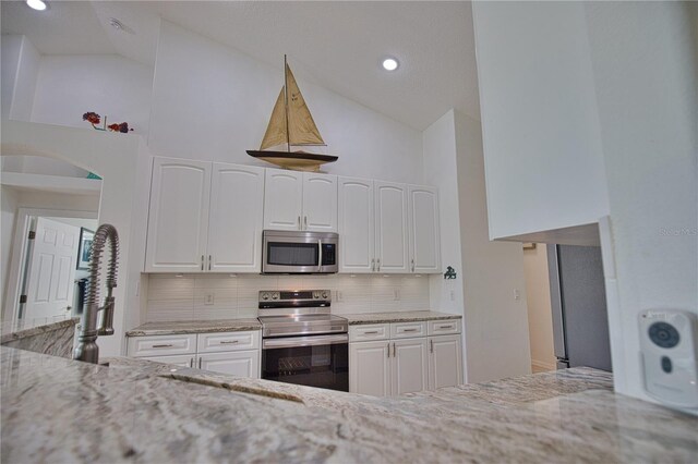 kitchen with backsplash, stainless steel appliances, white cabinets, and light stone countertops