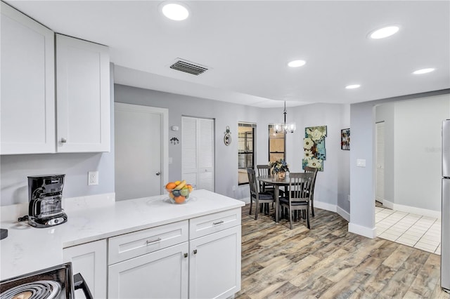 kitchen featuring light stone counters, light hardwood / wood-style floors, white cabinets, and hanging light fixtures