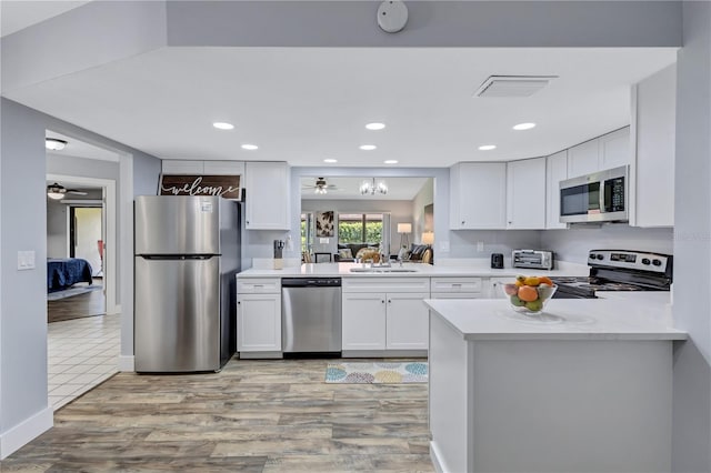 kitchen with white cabinets, light wood-type flooring, kitchen peninsula, and stainless steel appliances