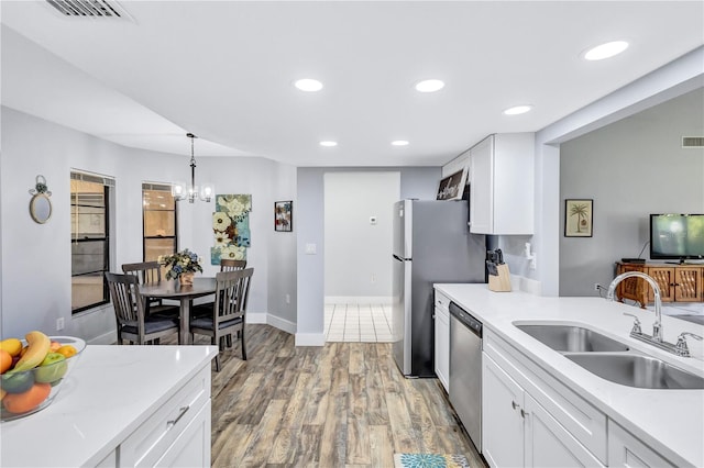 kitchen featuring stainless steel appliances, decorative light fixtures, sink, light wood-type flooring, and white cabinets