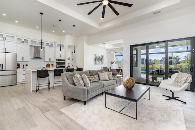 living room featuring light wood-type flooring, a tray ceiling, and ceiling fan