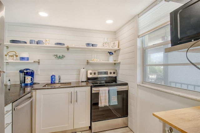 kitchen with sink, dark stone countertops, wooden walls, stainless steel appliances, and white cabinets