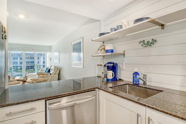 kitchen featuring sink, dark stone counters, stainless steel dishwasher, and white cabinetry