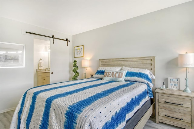 bedroom featuring a barn door, light hardwood / wood-style flooring, and ensuite bathroom