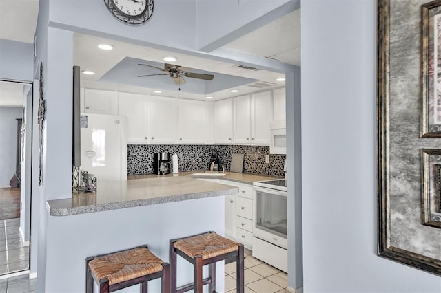 kitchen featuring white appliances, tasteful backsplash, a ceiling fan, a breakfast bar area, and white cabinetry