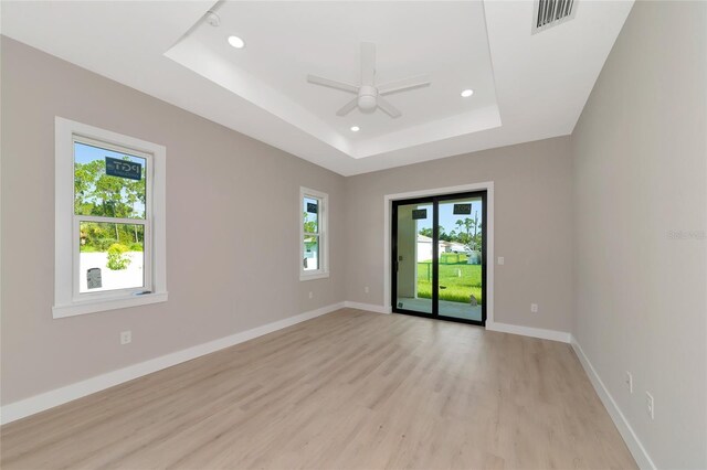 spare room featuring light wood-type flooring, a tray ceiling, and ceiling fan