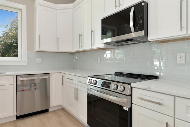 kitchen with stainless steel appliances, light wood-type flooring, white cabinetry, and decorative backsplash