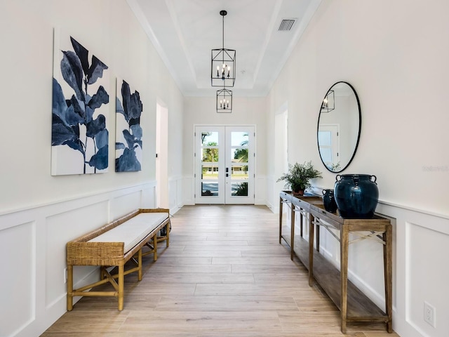 corridor featuring a notable chandelier, light hardwood / wood-style floors, a raised ceiling, and french doors