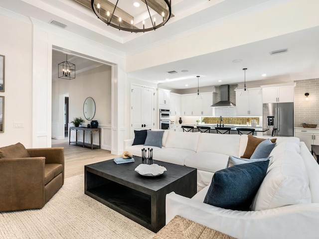 living room with a chandelier, light wood-type flooring, crown molding, and sink