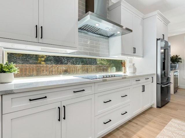 kitchen with light hardwood / wood-style flooring, wall chimney exhaust hood, black electric cooktop, high quality fridge, and white cabinetry