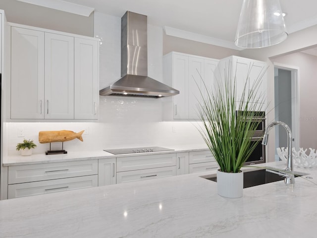 kitchen with light stone countertops, wall chimney range hood, white cabinets, and black electric cooktop