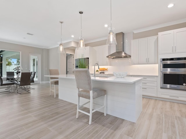 kitchen featuring wall chimney range hood, white cabinets, and a center island with sink