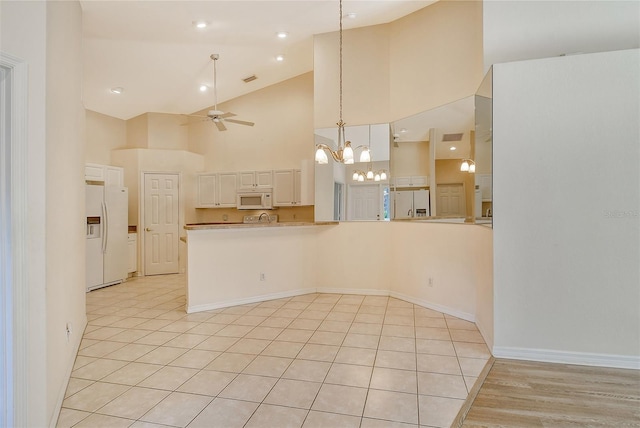 kitchen featuring white appliances, baseboards, light countertops, high vaulted ceiling, and ceiling fan with notable chandelier