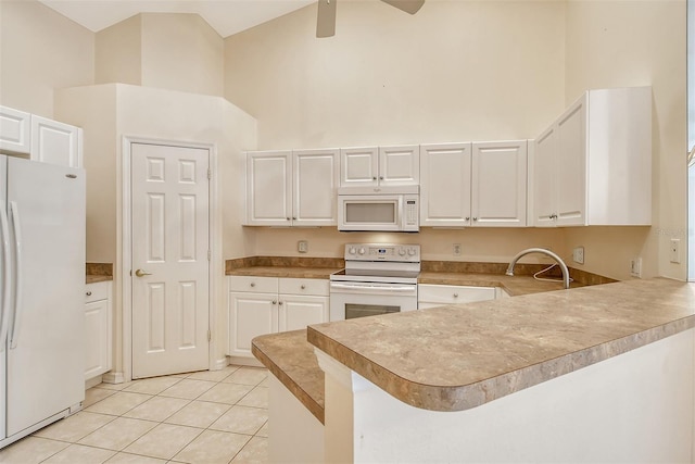 kitchen with white appliances, light tile patterned floors, a peninsula, a high ceiling, and white cabinetry