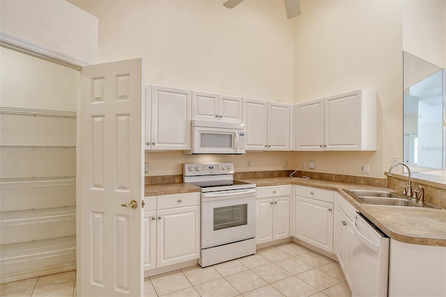 kitchen with white appliances, white cabinets, a towering ceiling, light countertops, and a sink