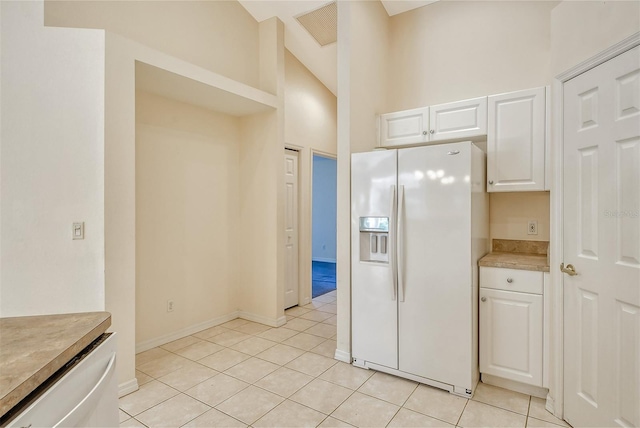 kitchen with light tile patterned floors, white refrigerator with ice dispenser, visible vents, light countertops, and white cabinetry