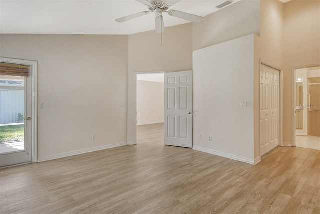 empty room featuring baseboards, visible vents, a towering ceiling, and light wood finished floors