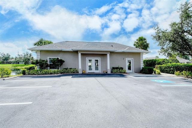 exterior space featuring a shingled roof, a water view, french doors, uncovered parking, and stucco siding