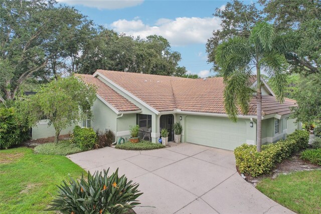 single story home featuring a garage, driveway, a tiled roof, a front lawn, and stucco siding